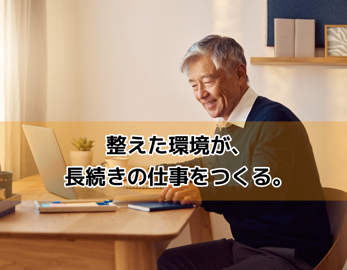 清潔に整えられたホームオフィスのデスク。ノートパソコン・コーヒー・観葉植物が置かれた木製デスクの前で、60代の日本人男性が作業環境を整えている。